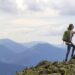 Young tourists with backpacks, athletic man helps slim woman to clime rocky mountain top against